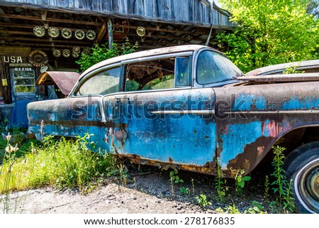 An Old Blue Rusted out car in front of a shed