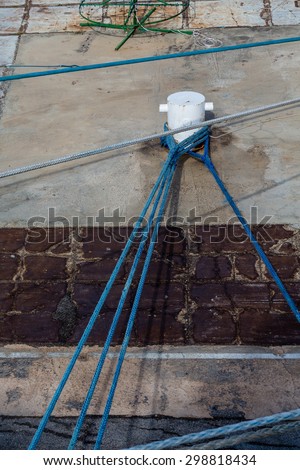 Ship\'s ropes tied to a metal bollard on a concrete pier