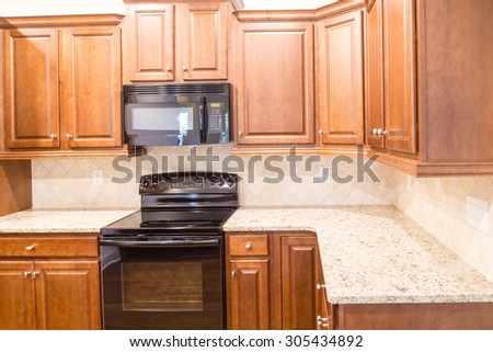 A New Kitchen with Granite Countertops and Black Appliances with wood cabinetry