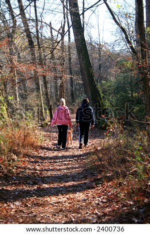A pair of women walking a dog down a forest path