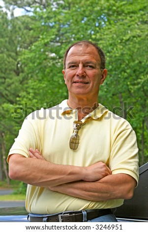 A confident older man in a yellow shirt leaning against his car