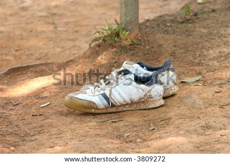 An old pair of dirty sneakers left in the dirt by a bench