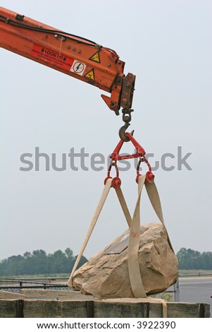 A construction crane lifting a heavy rock in place