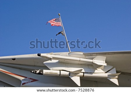 Missles under the wing of a fighter jet against blue sky with American flag and POW flag in background