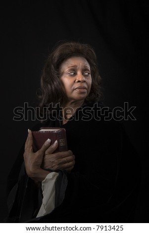 A woman holding a bible to her chest and looking to the left on black background