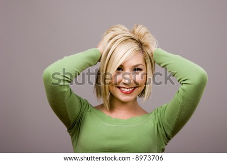 A blonde fashion model in a green blouse mussing her hair with her hands behind her head