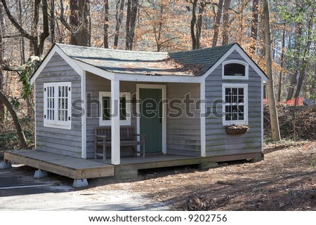 A small grey cabin in the woods with a porch and a green door