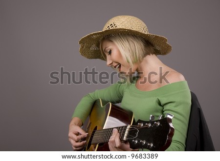 A blonde model in a straw hat and green blouse playing the guitar
