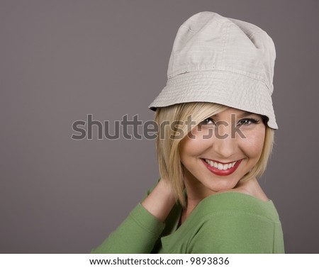 A blonde in a green blouse and silly white hat smiling with her hand behind her head