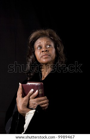 A black woman holding a bible and bright eyes turned to heaven