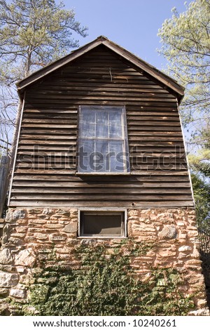 An old plank and log house on a stone foundation against a blue sky