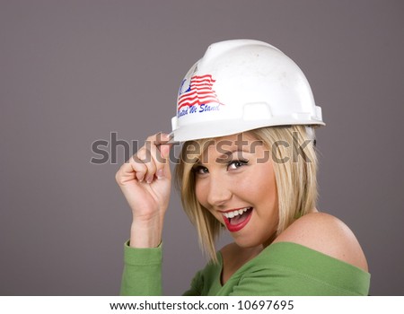 A blonde in a green blouse tipping a hard hat to the camera