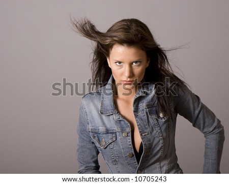 A woman with brown hair and a denim jacket unbuttoned with hair blowing in the breeze