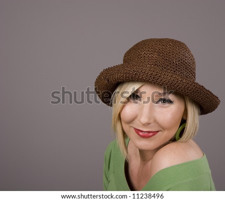 A blonde in a green blouse and a silly brown hat with a small smile