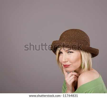 A blonde in a green blouse and silly brown hat with her finger on her lips