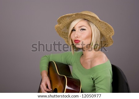 A blonde in a green blouse playing the guitar and puckering her lips