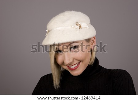 A blonde in a black turtleneck and white fur hat with a cute smile