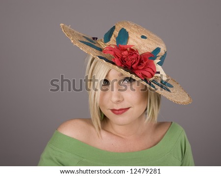 A blonde in green blouse with a flowered hat slanted and big eyes looking at the camera
