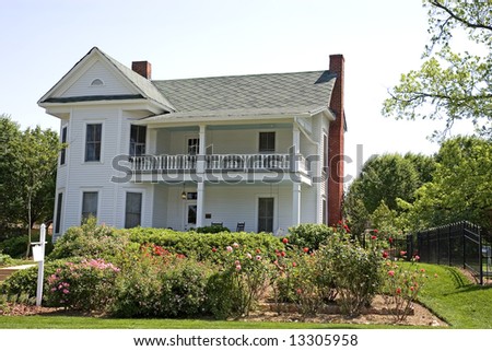 A white traditional colonial house behind a rose garden