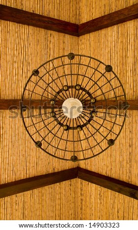 A bamboo and wood roof with a wrought iron light fixture