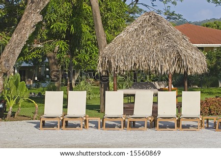 White lounge chairs and a straw hut around a tropical swimming pool