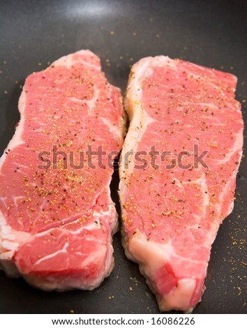 Seasoned strip steaks in a pan ready for cooking