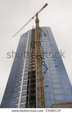 A blue high rise tower with yellow crane against sky