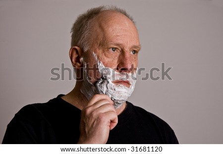An older bald man in a black shirt shaving