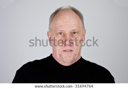 An older bald man in a black shirt looking stern