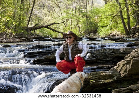 An hispanic man wearing orange pants in a river with his dog