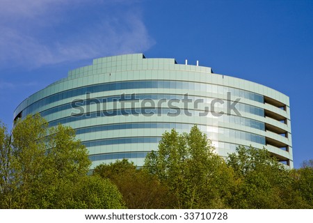 A green curved modern office building out of the trees against a blue sky