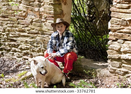 Hispanic Man in plaid shirt and orange pants with a dog by an old rock wall