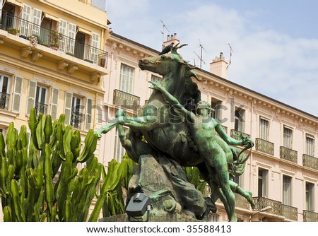 An old statue of a horse in front of a classic pink hotel in Cannes France