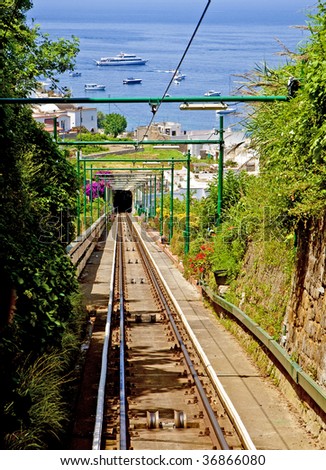 A tram track running down a steep hill into a tunnel toward a busy bay