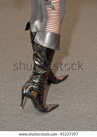 A woman wearing black shiny boots and torn pants