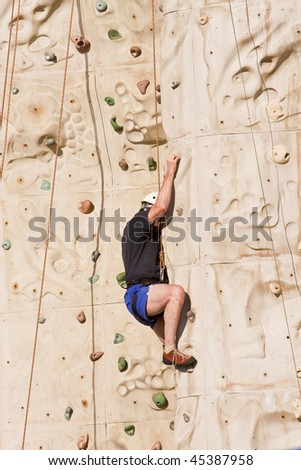A man stuck trying to climb a rock wall