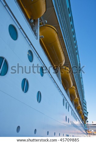 The side of a cruise ship with lifeboats and portholes