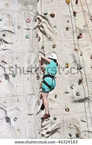 A middle aged woman climbing a rock wall with ropes and harness