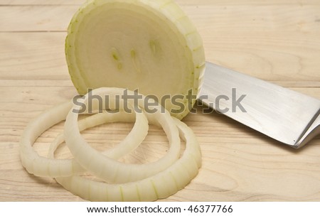 An onion being sliced on a wood cutting board