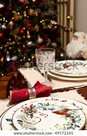 A dining table set for Christmas with a tree and Santa Claus in background