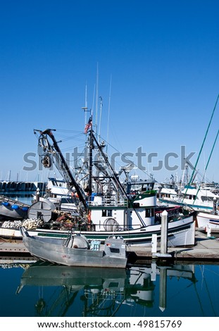 A small silver net boat docked by a large fishing trawler
