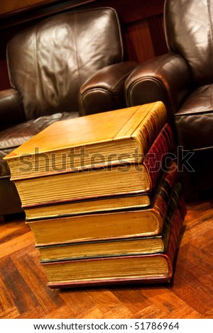 A stack of old books on a floor by leather chairs