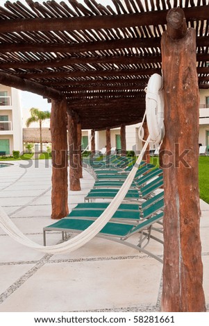 A white hammock hanging on a patio by chaise lounges