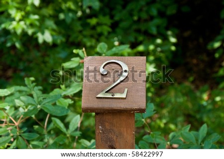 A brass number two on a wood mile marker on a woodland path