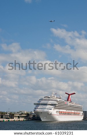 A luxury cruise ship at a port under a commercial airplane