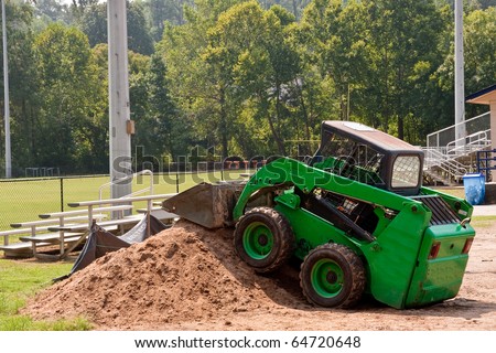 A small green earth moving machine on a dirt pile at a ball park