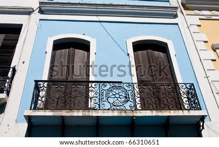 A black wrought iron railing on an old blue stucco building