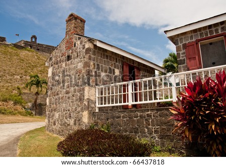 An old stone house with red shutters beneath a hilltop fort