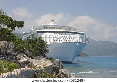 A white cruise ship anchored off the coast of the rocky coast of a tropical island