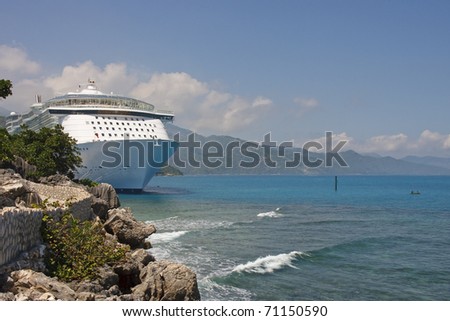 A huge white luxury cruise ship anchored near a rocky shore in the tropics